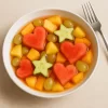 Bowl blanco con cóctel de frutas decorado con sandía en forma de corazón y pepino en forma de estrella