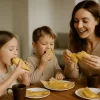 Madre con dos hijos comiendo tamales de elote dulce en una mesa con luz natural